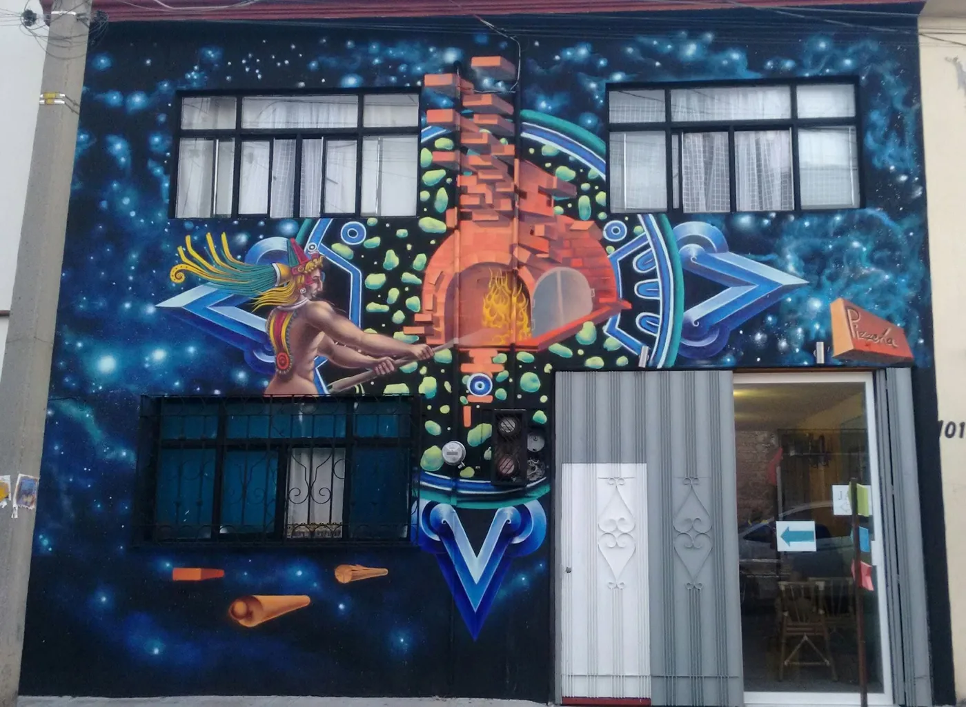 Fachada de la pizzería con un mural de un horno de leña y un cielo estrellado